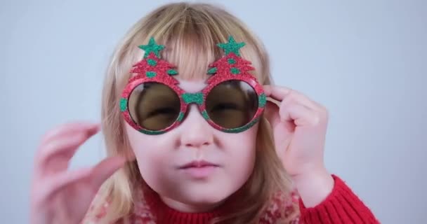 Emocionální překvapení malá blondýnka v novoroční brýle vypadá velmi zapůsobil na kameru — Stock video