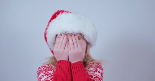 Schattig klein blond meisje in kerstman hoed met gesloten adem maakt een wens opent haar ogen. — Stockvideo