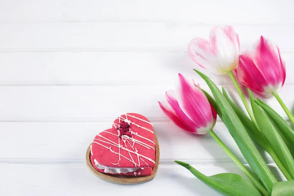 Colorful tulips and hearts cookie on white wooden background. — Stock Photo, Image
