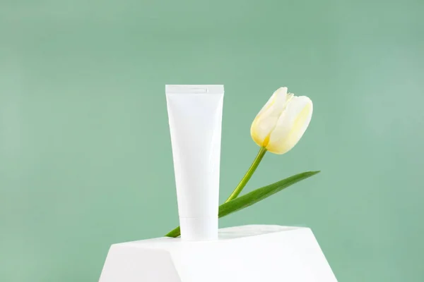 Tubo cosmético blanco con flor de tulipán en podio blanco — Foto de Stock