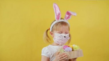 Tıbbi Maskeli Şirin Kız sarı arka planda paskalya yumurtasıyla dans ediyor..
