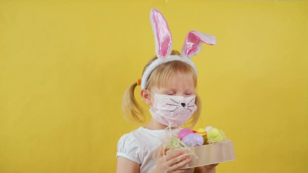 Cute Girl with Rabbit Ears In a Medical Mask dancing with easter egg on yellow background. — Stock Video
