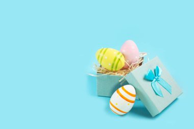 Mavi bir hediye kutusunda beyaz yuvada renkli Paskalya yumurtaları