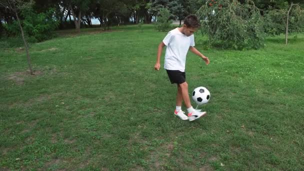 Мальчик-подросток играет в футбол на свежем воздухе, летом бросает мяч в парке. — стоковое видео