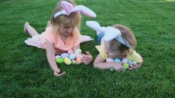 Mutlu küçük kız kardeşler yeşil çimenlerde yatar ve paskalya yumurtalarıyla oynarlar. . — Stok video