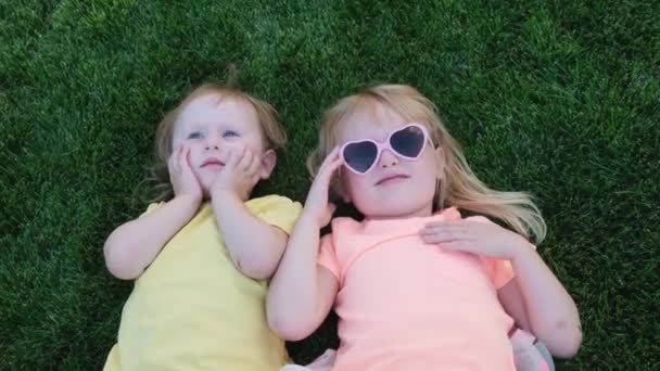 Щасливі маленькі сестри лежать на зеленій траві. старша сестра цілує її маленьку сестру . — стокове відео