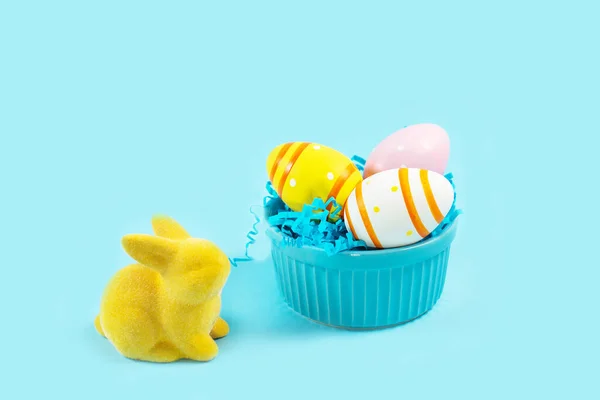 Yellow Easter bunny rabbit with painted egg on plate on blue background. — 스톡 사진