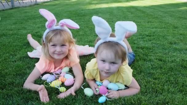 Szczęśliwe małe siostry leżą na zielonej trawie i bawią się wielkanocnymi jajami . — Wideo stockowe