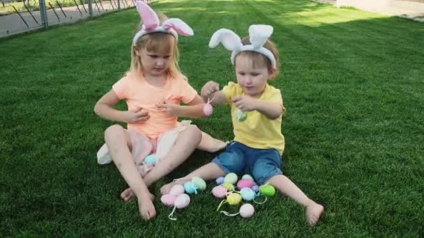 Happy little sisters sitting on the green grass and plays with easter eggs . — Stock Video