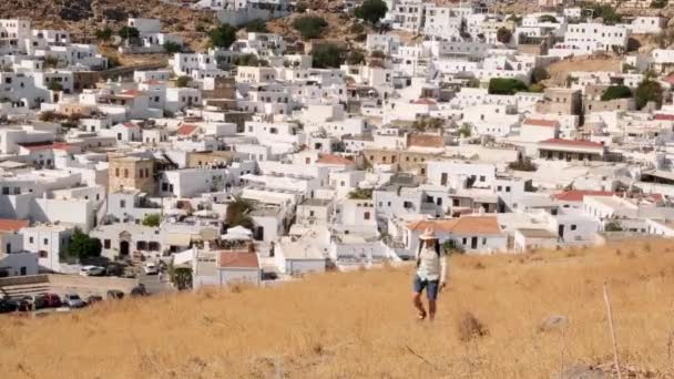Um turista caminha em uma colina com vista para a cidade de Lindos, Grécia — Vídeo de Stock