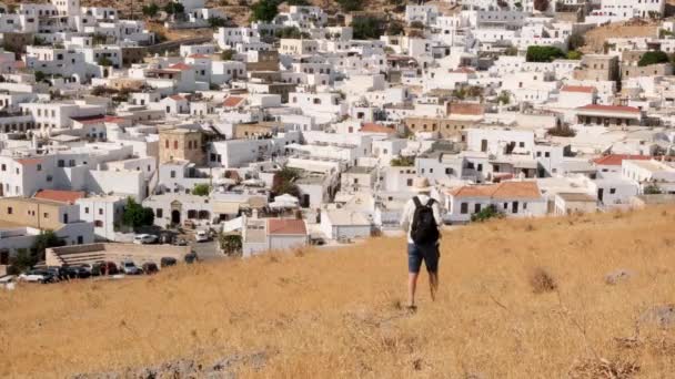 Турист іде по пагорбу з видом на місто Ліндо (Греція). — стокове відео