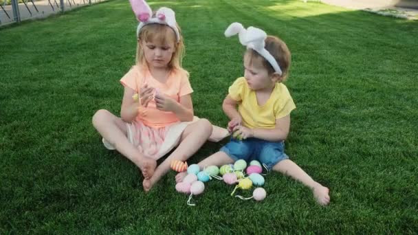Gelukkig zusjes zitten op het groene gras en spelen met paaseieren . — Stockvideo