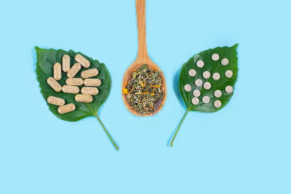 Pílulas orgânicas em folhas verdes e colher de madeira wiht herbals no fundo azul. Fotografias De Stock Royalty-Free