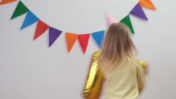 Happy Blonde caucasian kid girl in birthday hat keeps gold foil balloon number 5 and spinning around — Stock Video