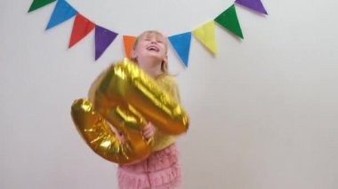 Doğum günü şapkalı mutlu sarışın beyaz kız altın folyo balonunu 5 numarada tutuyor ve eğleniyor..