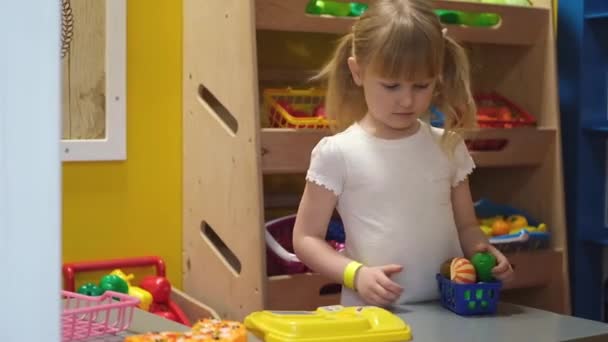 Feliz niña rubia preescolar jugando con la cocina de juguete en el centro de juegos para niños. Diversión en habitación de niños. — Vídeos de Stock