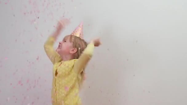 Niña feliz en sombrero de fiesta celebrando en fiesta de cumpleaños saltando con confeti — Vídeo de stock