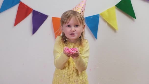 Щаслива дівчина в вечірці капелюх святкування на день народження вечірка blowing handful з барвиста confetti — стокове відео