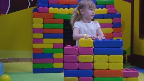 Preschool kid girl builds a house of colored plastic toy bricks. — Stock Video