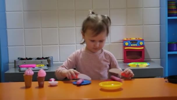 Щаслива дівчина дошкільного віку грає з іграшковою кухнею в дитячому ігровому центрі. Розваги в дитячій кімнаті . — стокове відео