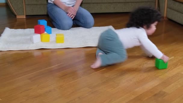 Gelukkig moeder en baby zoon spelen met blokjes op gezellig tapijt thuis, — Stockvideo