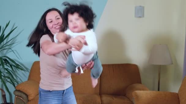 Happy young adult mom holding cute Mixed-race toddler little son holds and circling in living room. — Stock Video