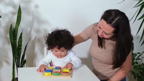 Mãe feliz ajudando adorável bebê menino menina ensinando pouco bebê aprendendo a jogar blocos de madeira na mesa em casa. — Vídeo de Stock