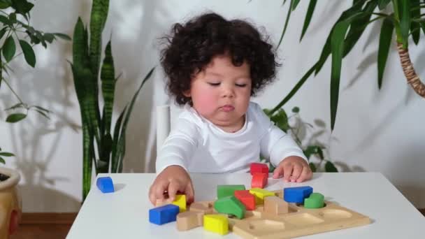 Niña de raza mixta niño pequeño se sienta a la mesa y apila juguetes de madera — Vídeo de stock