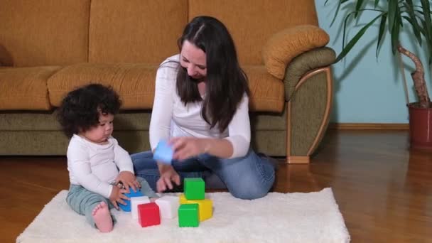 Feliz madre niñera y mixta-raza pequeño hijo jugando con cubos en acogedor alfombra en casa, — Vídeo de stock