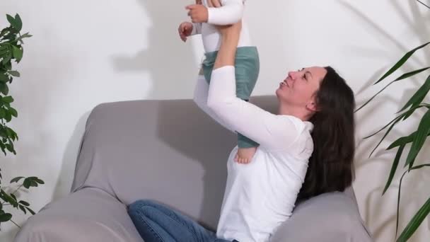 Joyeux petit garçon mignon jouant à s'amuser avec une jeune mère adulte sur le canapé à la maison — Video