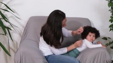 Mutlu küçük çocuk evde kanepede genç yetişkin annesiyle eğleniyor.