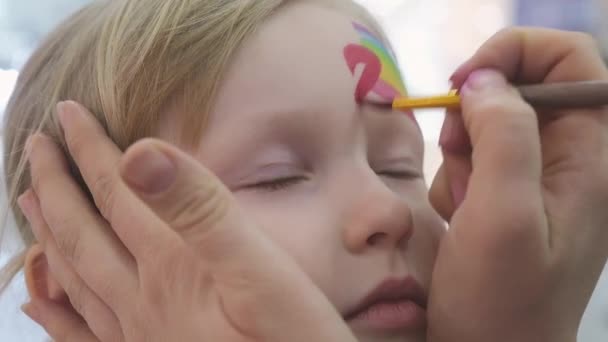 Artysta maluje tęczę i serce na twarzy dziewczyny. — Wideo stockowe