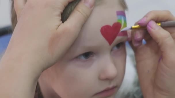 Artista pintando um arco-íris e coração no rosto das meninas. — Vídeo de Stock