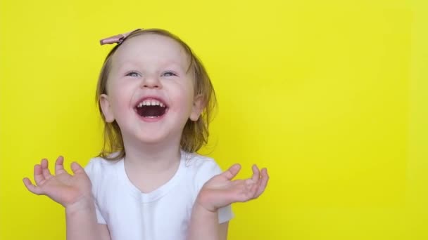 Zabawna dziewczynka uśmiecha się patrząc na kamerę na żółtym tle. . — Wideo stockowe