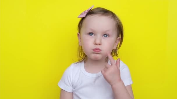Graciosa niña pequeña hinchó sus mejillas y luego los sopla mientras mira a la cámara en el fondo amarillo. — Vídeos de Stock