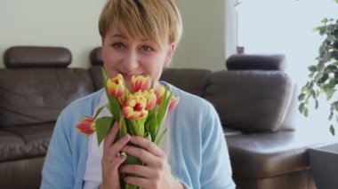 Mutlu kadın lale buketi tutuyor ve evdeki kameraya gülümsüyor..
