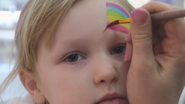 Kunstenaar schilderen een regenboog op meisjes gezicht. — Stockvideo