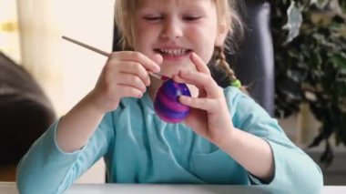 Happy preschool cute girl, decorate eggs with paints. Preparation for Easter.
