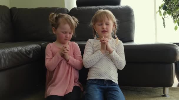 Little girls are praying to God in the living room crossed their arms and stand on kneel. — Stock Video