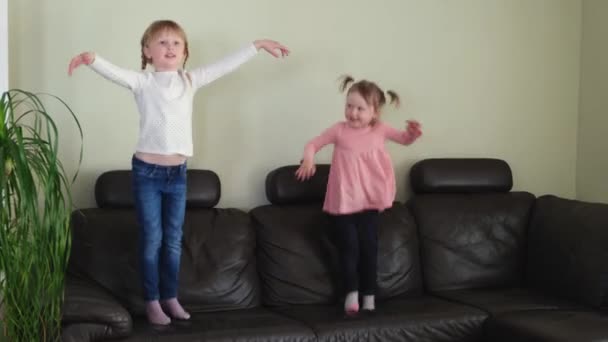 Happy Active toddler girls jumping on the couch in the living room at home. — Stockvideo