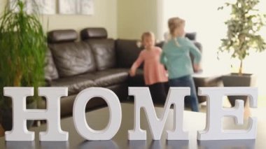 Cute little girls kids jumping dancing in modern house living room and large letters with the inscription HOME.
