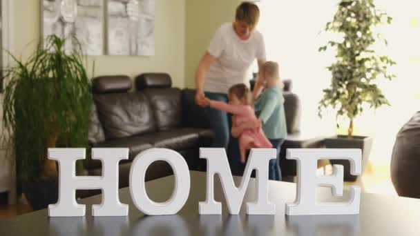 Aktív anya és aranyos kisgyerekek lánya forog a táncban a nappaliban a háttérben a felirat HOME — Stock videók