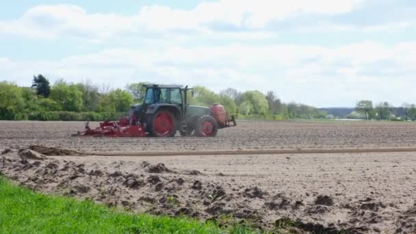 Boer in tractor ploegt een veld in het voorjaar. Zijaanzicht van de rode boerderij machine met apparatuur. — Stockvideo