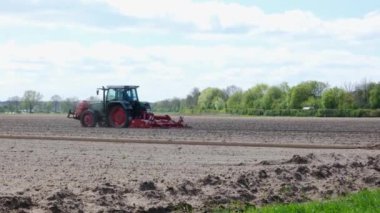 İlkbaharda traktörlü bir çiftçi tarlayı sürüyor. Ekipmanlı kırmızı çiftlik makinesinin yan görüntüsü.