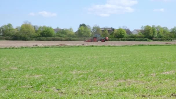 Boer in rode trekker ploegt een veld in het voorjaar. Zijaanzicht van de rode boerderij machine met apparatuur. — Stockvideo