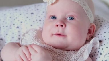 Mavi evetlerle güzel küçük bir kız çocuğu, yatağa uzanıp kameraya gülümsüyor. Yaşamın ilk yılındaki çocuk gelişimi. Çocukların korunması, evlat edinme, bebeklik kavramı