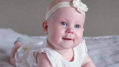 Sevimli küçük bir kız bebek yatakta yüzüstü yatar ve kameraya bakar ve gülümser. Erken bebek gelişimi.