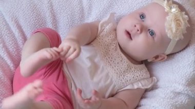 Mavi evetlerle güzel küçük bir kız çocuğu, yatağa uzanıp kameraya gülümsüyor. Yaşamın ilk yılındaki çocuk gelişimi. Çocukların korunması, evlat edinme, bebeklik kavramı