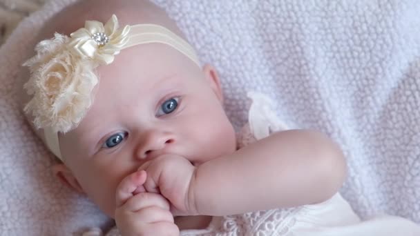青い目の女の子は居心地の良いベッドの上に横たわると彼女の指を吸うと カメラを見て 拳をクリックします 赤ちゃんの歯の概念 顔を閉じて — ストック動画