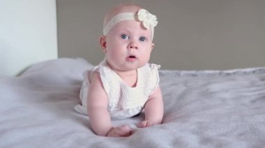 Sevimli küçük bir kız bebek yatakta yüzüstü yatar ve kameraya bakar ve gülümser. Erken bebek gelişimi.